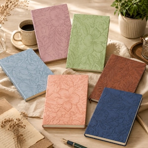 May include: A collection of six rectangular notebooks featuring embossed floral patterns on their covers. The notebooks are available in pink, light green, light blue, peach, brown, and dark blue, each displaying detailed hibiscus flower designs.