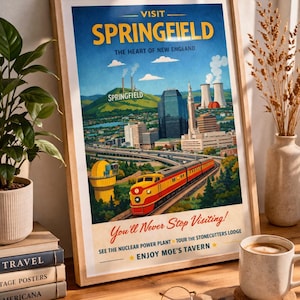 May include: Framed vintage travel poster for Springfield, featuring a train, city skyline, and text that reads "You'll Never Stop Visiting!" The poster is displayed on a wooden desk with books, a coffee mug, and eyeglasses.