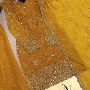 May include: Mustard yellow embroidered ensemble featuring a long-sleeved tunic and matching scarf. The tunic is adorned with intricate silver embroidery and sequins, with detailed patterns on the sleeves and hem. The scarf has a delicate border.