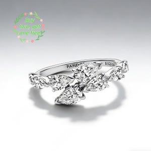 Puede incluir: Un anillo de plata con múltiples piedras preciosas claras en forma de pera. El anillo tiene la inscripción "PANDORA". También es visible el texto "S925 AU". La imagen también contiene el texto "Buy two, get one free".