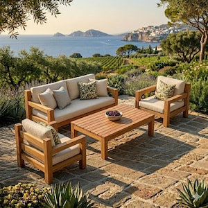 May include: Outdoor patio furniture set with a sofa, two armchairs, and a coffee table. The wooden frames have beige cushions and patterned throw pillows. The coffee table holds a bowl of fruit. The set is on a stone patio with a scenic ocean view.