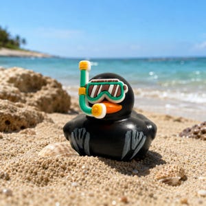 May include: A black rubber duck toy wearing a green and white snorkel mask with an orange beak. The duck features painted gray wing details on its sides and is positioned upright. The snorkel mask has a green frame and a white mouthpiece.