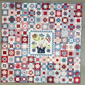 May include: A square patchwork quilt featuring a red, white, and blue color scheme. The quilt is composed of numerous small blocks with star and floral patterns. A central white square displays a dark blue pot with flowers and an American flag.