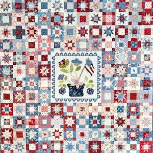 May include: A patchwork quilt featuring a grid of red, white, and blue fabric squares with star and floral patterns. The center square displays an applique of a dark blue flower pot containing flowers and a small American flag on a pole.