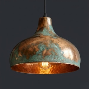May include: A copper pendant light with a distressed finish. The dome-shaped shade features a mix of copper and verdigris green hues, with a warm, glowing interior. The light hangs from a black cord, showcasing an exposed bulb.