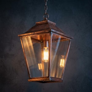 May include: A copper-colored, rectangular pendant light fixture with clear glass panels. The light has a vintage-style Edison bulb and is suspended by a chain. The fixture has a textured finish and is designed for indoor use.