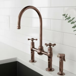 May include: A copper-coloured kitchen tap with a high-arc spout and cross-handle design. The tap includes a side sprayer and is set against a white tiled backsplash and a dark sink.
