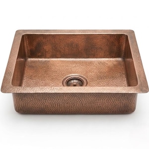 May include: A square copper sink with a hammered texture. The sink has a rectangular basin and a drain in the center. The copper has a warm, reddish-brown hue, and the edges are slightly rounded.