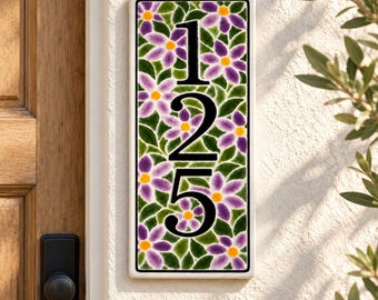 May include: A rectangular ceramic house number plaque featuring the black digits 125 vertically aligned. The background is decorated with a repeating pattern of purple flowers with yellow centers and green leaves on a white base.