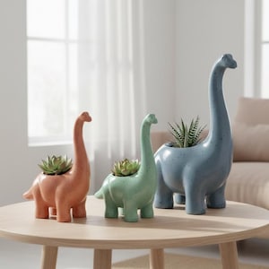 May include: Three ceramic dinosaur planters in coral, mint green, and blue-gray, each holding a succulent plant. The planters are on a light wood table, with a neutral background.