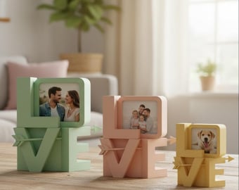 Può includere: Tre portafoto decorativi dai colori pastello che compongono la parola "LOVE". Ogni cornice contiene una fotografia e presenta una freccia che attraversa la "V". Le cornici sono nelle tonalità del verde, del rosa e del giallo.