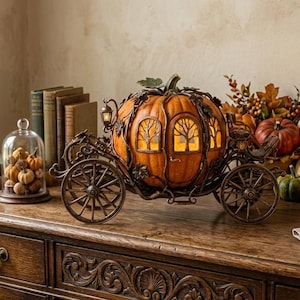 May include: An orange pumpkin carriage with decorative metalwork, lit windows, and a green stem sits on a wooden surface. The carriage is surrounded by pumpkins, candles, and fall foliage, creating an autumnal display.