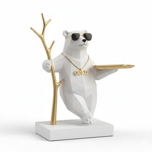 May include: A white geometric polar bear figurine wearing sunglasses and a gold chain with the word "GOLD". The bear holds a gold tray and a gold branch. The figurine is on a white base.