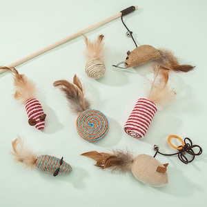May include: A selection of cat toys in different shapes and colours. Includes a wooden wand with a feather and bell, a hessian mouse, and several toys with feathers and striped or spiral designs. The toys are designed to encourage play.