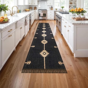 以下が含まれることがあります： ベージュの幾何学模様が施された、長いダークグレーのランナーラグ。 ラグの中央にはひし形と円形の模様が並び、側面には矢印のような模様があります。 フリンジの縁があり、木製の床に置かれています。