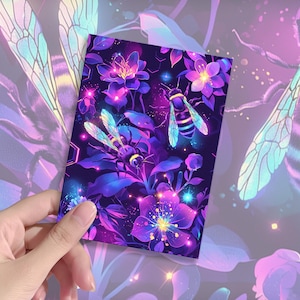 Op de afbeelding: Een rechthoekige kaart met een levendige illustratie van bijen en bloemen in paarse, blauwe en gele tinten. Het ontwerp toont gedetailleerde bijen met iriserende vleugels en gloeiende accenten, tegen een bloemenachtergrond. De kaart wordt door een hand vastgehouden.