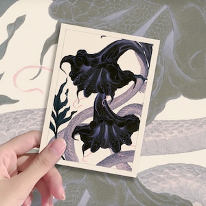 May include: A rectangular art print featuring two large, dark purple and black trumpet-shaped flowers with intricate petal details. The floral illustration is set against a light cream background and includes thin, winding, light-coloured snake-like forms.
