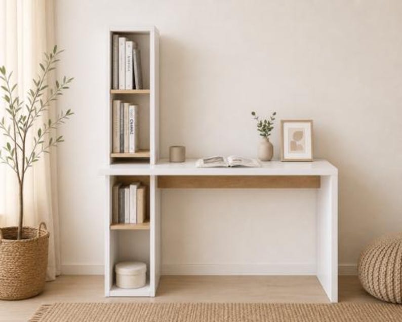 May include: A modern white desk with a built-in bookshelf. The desk has a light wood accent and is paired with a woven pouf and a potted plant. Books and decorative items are arranged on the desk and shelves.