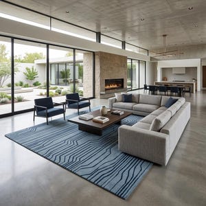 Peut inclure: Un grand tapis rectangulaire présentant une base bleu clair avec des motifs linéaires bleu foncé. Le tapis est placé sous une table basse en bois foncé, deux fauteuils bleu foncé et un grand canapé d'angle gris clair dans une pièce spacieuse.
