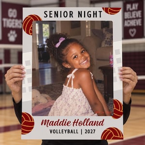 May include: A rectangular photo frame prop for Senior Night featuring a white border with maroon volleyball graphics. The top text reads SENIOR NIGHT and the bottom text reads Maddie Holland VOLLEYBALL | 2027. The frame displays a photo of a child.