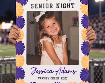 Puede incluir: Un marco de fotos rectangular con un borde de pompones morados y amarillos. El texto superior dice SENIOR NIGHT. El texto inferior muestra el nombre Jessica Adams, seguido de VARSITY CHEER | 2027. El centro contiene una fotografía.