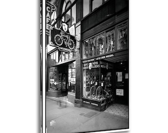 Tableau vintage en noir et blanc représentant une scène de rue avec un magasin de vélos et un serrurier. Décoration murale pour le salon ou la maison.