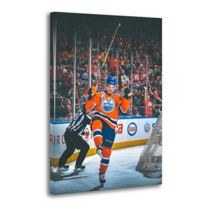 May include: Canvas print of an Edmonton Oilers hockey player celebrating a goal. The player is wearing an orange and blue jersey with the Oilers logo. The background shows a crowd of fans and the hockey rink.