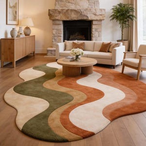 May include: An area rug featuring a large, organic, wavy shape with wide, flowing bands of color in olive green, mustard yellow, cream, and burnt orange. The rug has a soft, textured pile and is positioned on a light-toned wooden floor.