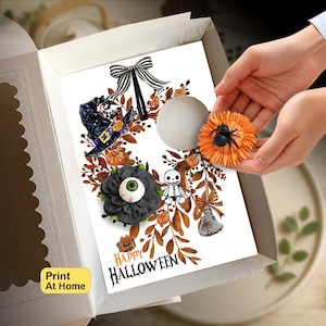 Puede incluir: Una tarjeta rectangular blanca con una ilustración de corona de Halloween que incluye un lazo a rayas blanco y negro, un sombrero de bruja, un esqueleto, una escoba y flores naranjas y negras. El texto dice Happy HALLOWEEN y Print At Home.