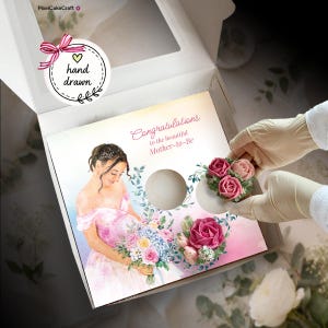 Puede incluir: Una caja de cartón blanco que contiene una tarjeta cuadrada con una ilustración en acuarela de una persona embarazada con un vestido rosa sosteniendo flores, con el texto Congratulations to the beautiful Mother-to-Be y dos recortes circulares.