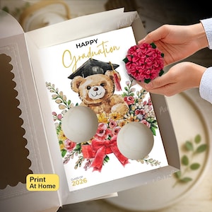 May include: A white cardboard box containing a rectangular card with the text Happy Graduation and Class of 2026. The card features a watercolour illustration of a teddy bear wearing a graduation cap, surrounded by flowers and a red bow.