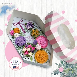 May include: A coffin-shaped gift box containing an assortment of colorful floral-shaped cupcakes. The box lid features pink and white stripes. The interior base displays a printed floral design with the text Happy Birthday and a purple ribbon.
