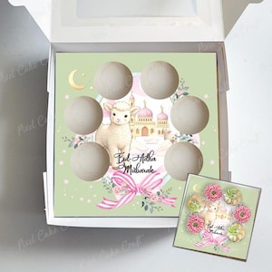 Puede incluir: Una caja decorativa con fondo verde que presenta un cordero, una mezquita y el texto "Eid Adha Mubarak". La caja contiene seis golosinas redondas de color claro. También se ve una caja más pequeña con golosinas similares.