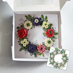 Pode incluir: Um bolo com um design de coroa de flores, com flores de creme de manteiga vermelhas, brancas, roxas e amarelas. O bolo está numa caixa branca com tampa transparente. Uma imagem menor está no canto.