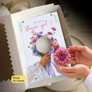 May include: A white card inside an open box featuring a watercolor illustration of a hand holding a bouquet of colorful flowers with the text Will you be my flower girl? A circular cutout in the center allows for a pink dahlia flower to be attached.