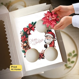 Könnte beinhalten: Ein weißer Karton mit einer bedruckten Karte, die einen Weihnachtskranz, eine Weihnachtsmann-Illustration und den Text Merry Christmas zeigt. Die Karte hat drei kreisförmige Ausschnitte und eine rote Weihnachtsstern-Blüte oben.