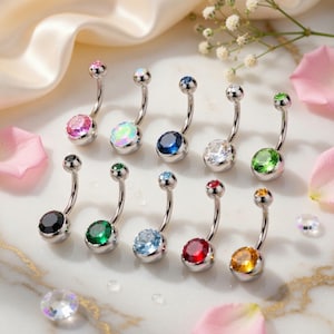 May include: A selection of curved belly button rings with different coloured gemstones. The jewellery features a silver-coloured curved barbell with a small gem at the top and a larger, colourful gem at the bottom. Gem colours include pink, opal, blue, clear, green, black, and red.
