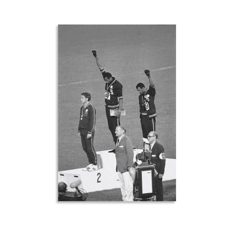 May include: Black and white photograph of the 1968 Olympics medal ceremony. Two athletes stand on the podium with raised fists, while another stands with a medal. Officials and a podium are also visible.
