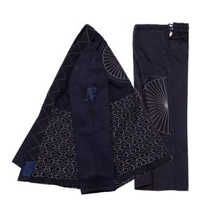 May include: Navy blue jacket and trousers set with white embroidered patterns. The jacket features a stylized "P" logo and geometric designs. The trousers have a drawstring waist and matching embroidery. The set is made of a dark fabric.