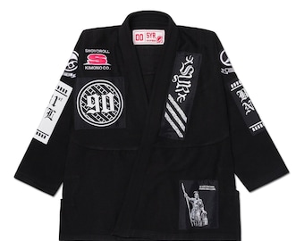 May include: Black Jiu-Jitsu gi with multiple patches. Patches include the text "SHOYOROLL KIMONO CO.", "90", and "SUR". The gi also features a graphic of a Roman soldier and the text "SI VIS PACEM PARA BELLUM".