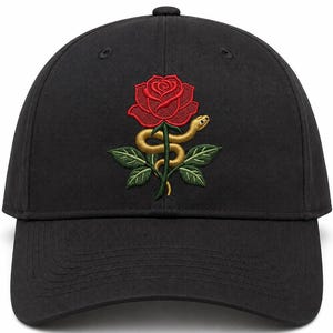 Puede incluir: Una gorra de béisbol negra con un diseño bordado en la parte frontal. El bordado muestra una rosa roja vibrante con hojas verdes y una serpiente de color amarillo dorado enroscada alrededor del tallo de la flor. La gorra es estructurada.