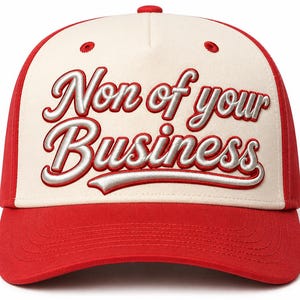 Puede incluir: Una gorra de béisbol roja y crema con el texto bordado "Non of your Business" en una fuente cursiva de tono plateado en el panel frontal. La gorra tiene una corona estructurada, una visera curva y ojales rojos en la sección frontal color crema.