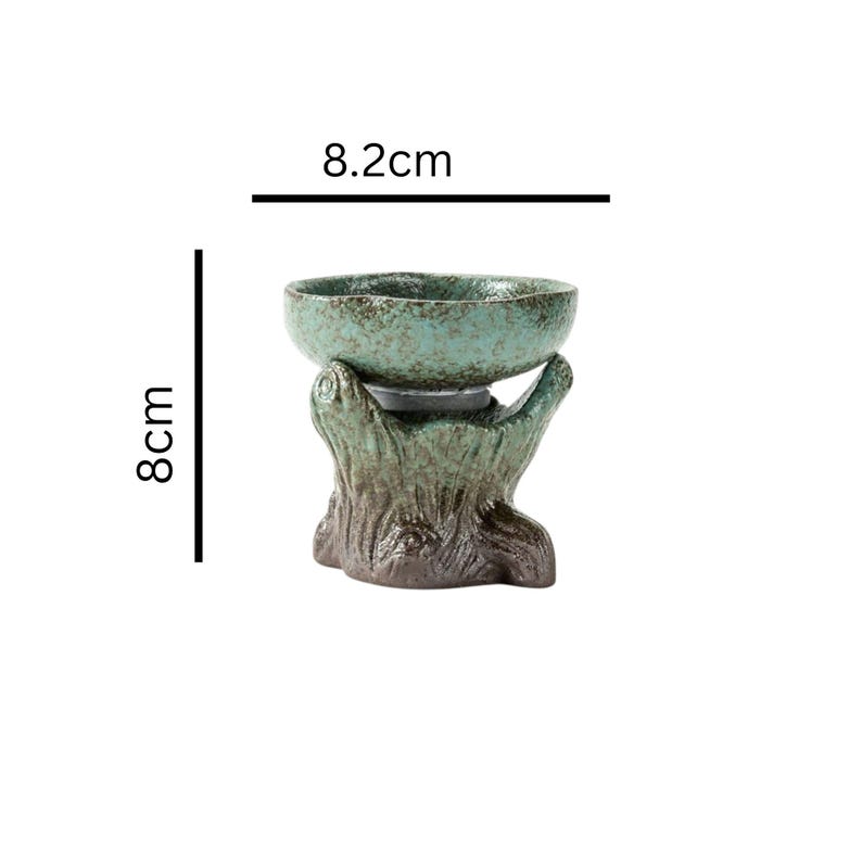 May include: A teal ceramic bowl, 8 cm tall and 8.2 cm wide, sits atop a tree trunk-shaped base. The bowl has a speckled finish, and the base is textured with shades of brown and green.