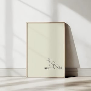 May include: A framed art print featuring a minimalist line drawing of a person and two objects. The artwork is in black against a cream background, set within a light wood frame. The print is leaning against a white wall, with shadows.