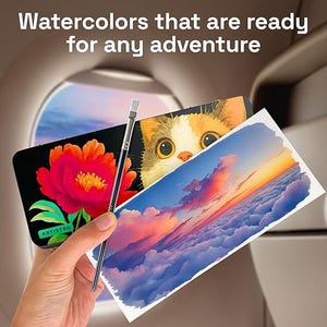 May include: A black watercolor paint set case featuring a red flower and a cat illustration, held alongside a paintbrush and a rectangular paper with a sunset cloud painting. The text reads: Watercolors that are ready for any adventure.