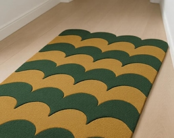 Puede incluir: Una alfombra rectangular con un patrón repetitivo de formas festoneadas verdes y doradas. La alfombra está colocada sobre un suelo de madera clara en un pasillo, añadiendo un elemento decorativo al espacio.