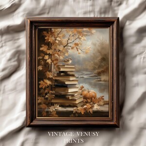 May include: A framed print featuring a stack of books with a bird perched on top, set against a backdrop of autumn foliage and a serene lake. A pumpkin rests near the books. The frame is dark brown. The text "VINTAGE VENUSY PRINTS" is at the bottom.