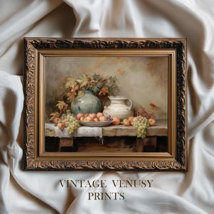 Può includere: Una stampa vintage incorniciata di natura morta con un tavolo con frutta, uva e due vasi in ceramica. La stampa ha una cornice dorata ornata e il testo "VINTAGE VENUSY PRINTS" in basso.