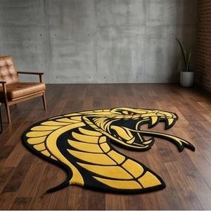 Può includere: Un tappeto sagomato che presenta un design a testa di cobra stilizzata in giallo vibrante e nero. Il serpente è raffigurato con la bocca aperta, zanne visibili e lingua biforcuta, creando un rivestimento per pavimenti grafico e audace.