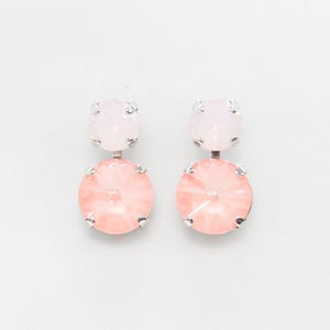 May include: A pair of drop earrings with a light pink and peach color scheme. Each earring features a small, round, light pink crystal at the top and a larger, oval, peach-colored crystal below, all set in a silver-tone metal.